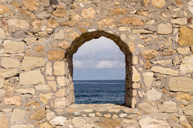 Hintergründe Die Textur der naturbraunen Steinwand mit Fenster- und Meerblick in der Nähe