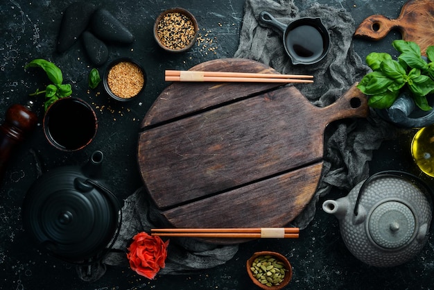 Hintergrund asiatischer Speisen: Teller, Stöcke und Gewürze auf schwarzem Steinhintergrund.