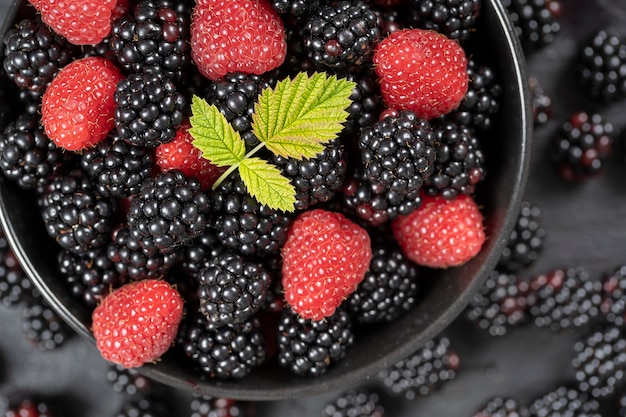 Hintergrund aus frischen Bio-Brombeeren und Himbeeren, Nahaufnahme. Viele reife saftige Wildfrüchte rohe Beeren in einem schwarzen Teller. Draufsicht Brombeere und Himbeere