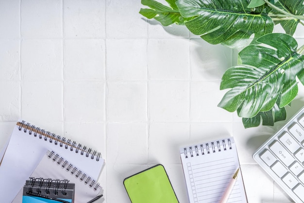 Hintergrund des Schreibtisches Laptop Tastatur Smartphone und verschiedene Arbeitsmaterialien auf dem weißen Schreibtisch Hintergrund Flatlay Kopierbereich