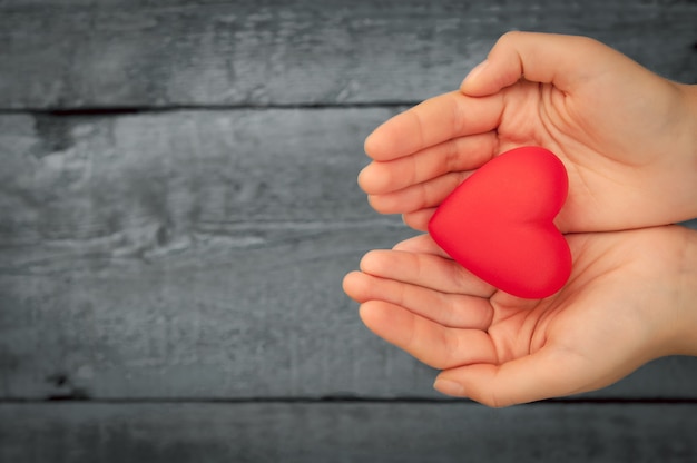 Foto hintergrund für den valentinstag. rotes herz in den händen. herzanhänger. rotes herz. platz für text.