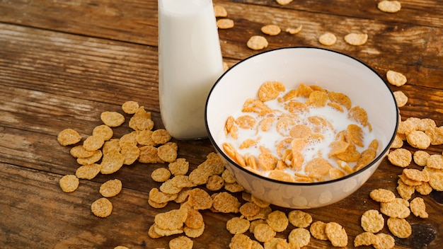 Hintergrund für gesunde Ernährung. Frische Milch in Schüssel mit Cornflakes. Hölzerner Hintergrund. Milch in einer Glasflasche