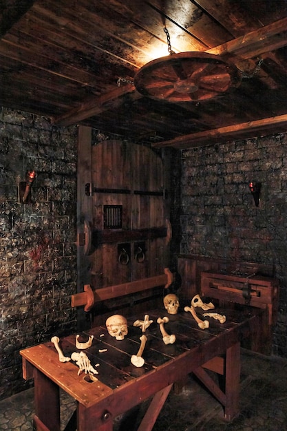 Hintergrund im mystischen dunklen Innenraum des mittelalterlichen Burgzimmers mit Holztisch mit Schädeln und Knochen gegen eine alte Steinmauer mit Tür
