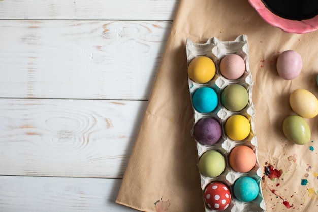 Hintergrund mit bunt gefärbten Ostereiern in einem Karton auf einem weißen Holztisch