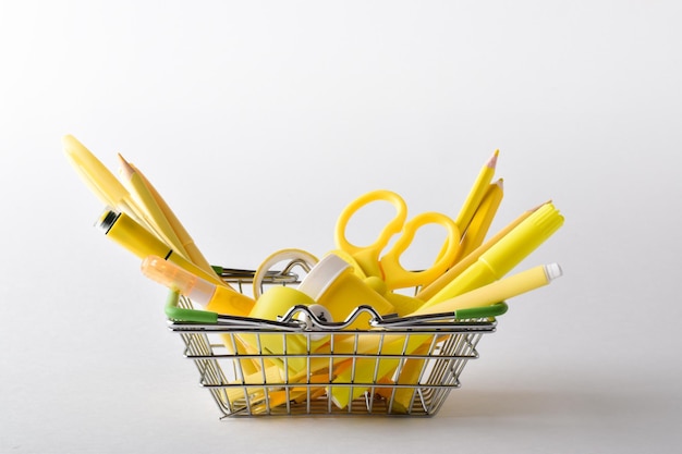 Hintergrund mit einem Metallkorb aus einem Supermarkt mit verschiedenen gelben Schreibwaren auf weißem Hintergrund