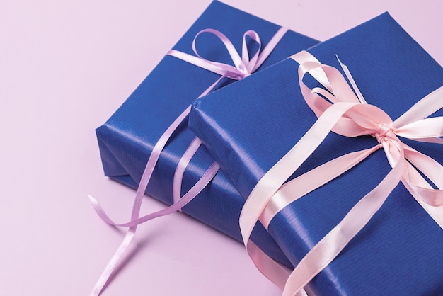 Hintergrund mit Geschenkboxen im blauen Geschenkpapier mit Bändern, die auf einem rosa Hintergrund liegen