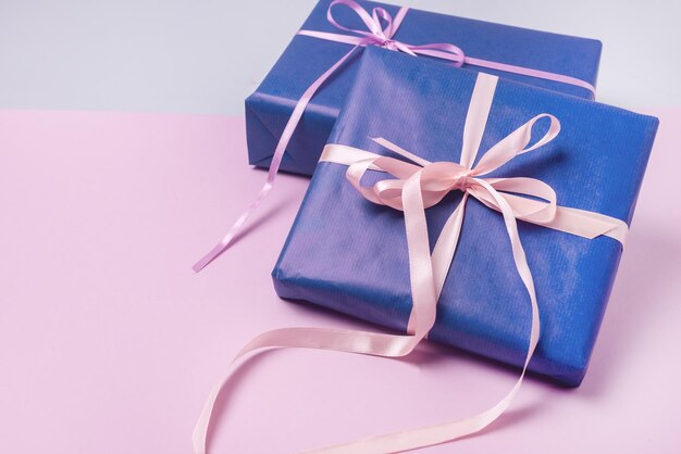 Hintergrund mit Geschenkboxen im blauen Geschenkpapier mit Bändern, die auf einem rosa Hintergrund liegen