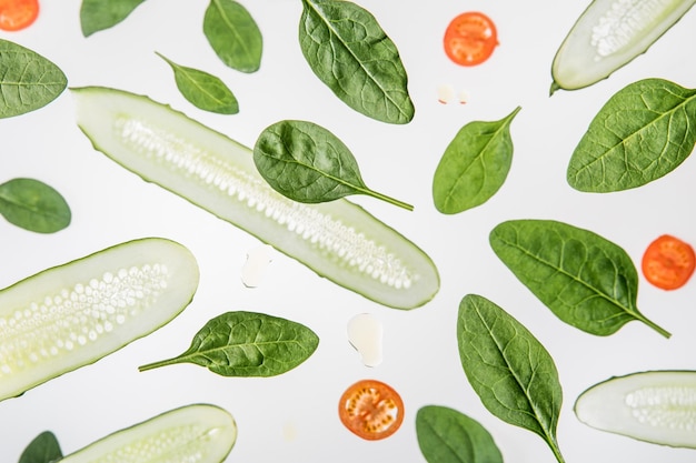 Hintergrund mit geschnittenen roten Tomaten, Spinatblättern und Gurken auf Grau