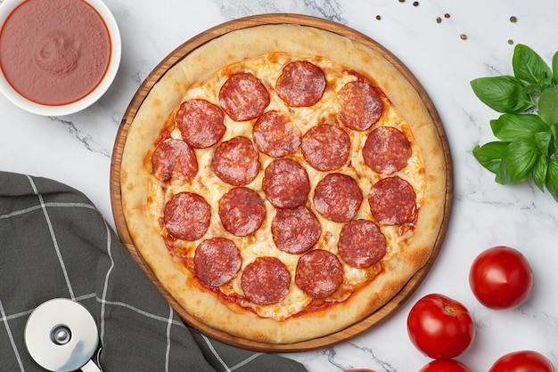 Hintergrund mit Peperoni-Pizza auf einem Holzbrett auf grauem Hintergrund mit Zutaten und Messer