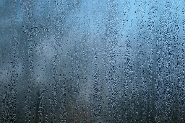 Hintergrund mit Regentröpfchen auf Fensterglas an düsteren Herbsttagen auf unscharfem blauem Hintergrund aus nächster Nähe