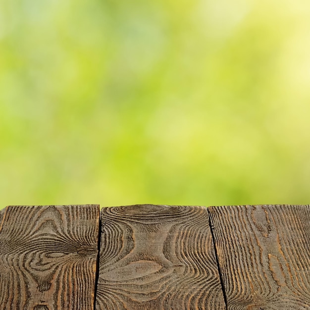 Hintergrund mit verschwommenen grünen Blättern und leeren Holzbohlen im Vordergrund