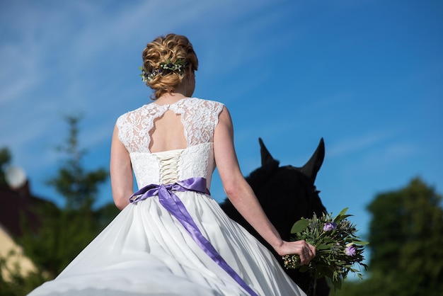 Foto hintergrundansicht der braut, die einen blumenstrauß hält, während sie auf einem pferd gegen den himmel reitet