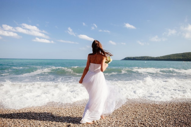 Hintergrundansicht der Braut mit Blumen am Strand an einem sonnigen Tag