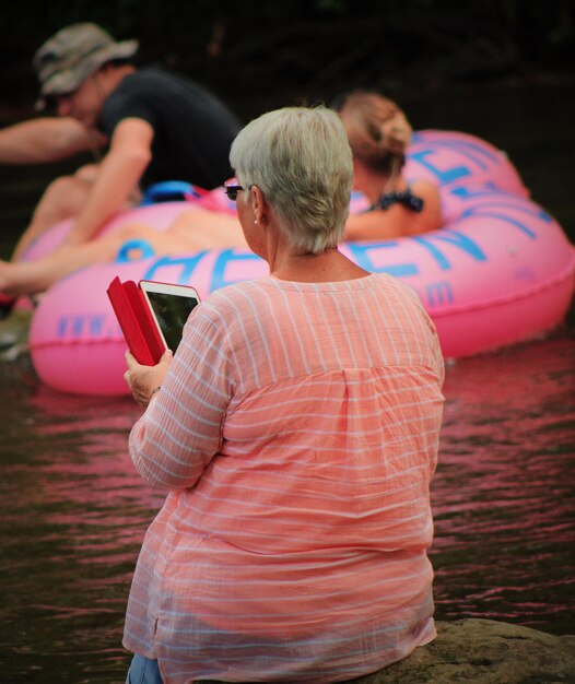 Foto hintergrundansicht einer älteren frau, die ein tablet gegen menschen benutzt, die im see schwimmen