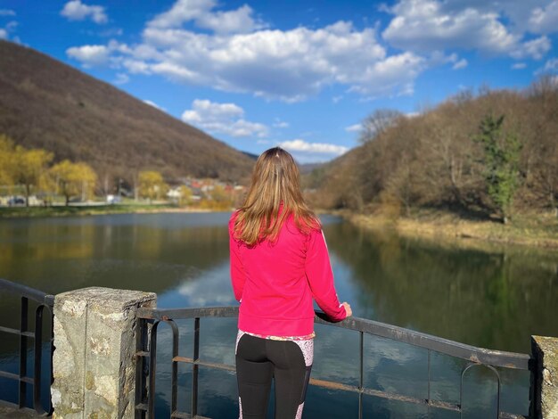 Foto hintergrundansicht einer blonden frau, die auf der brücke steht und den von wald umgebenen see betrachtet