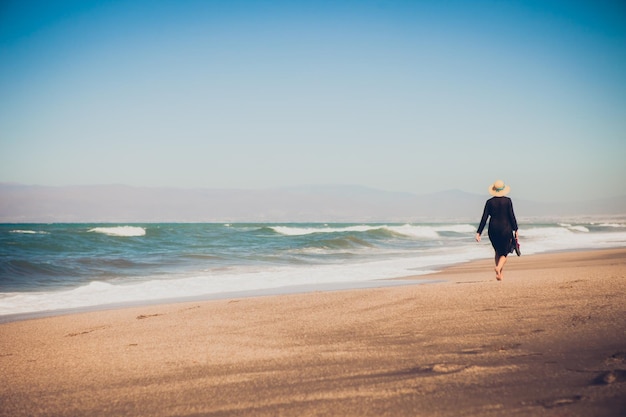 Hintergrundansicht einer Frau, die am Meer an einem klaren Himmel spazieren geht