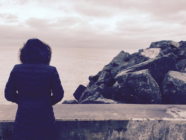 Hintergrundansicht einer Frau, die am Meer gegen einen bewölkten Himmel steht