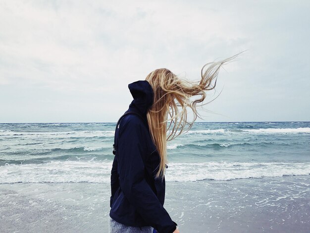 Hintergrundansicht einer Frau, die am Strand gegen den Himmel steht