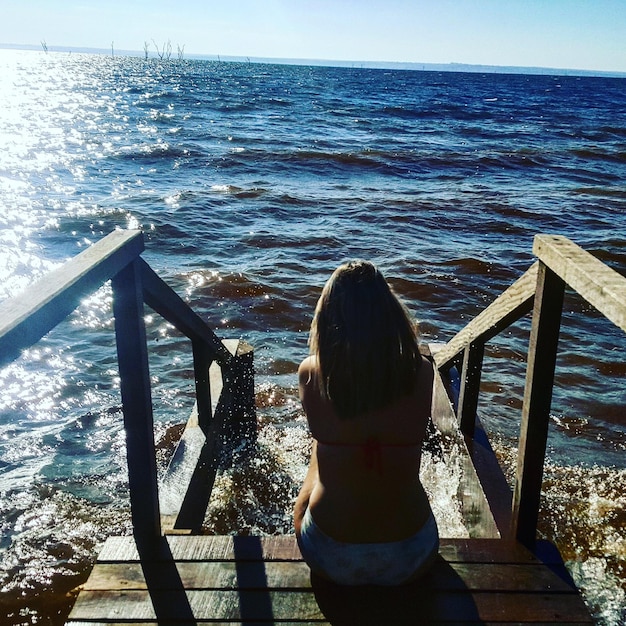 Hintergrundansicht einer Frau, die an einem Strand auf einer Treppe sitzt