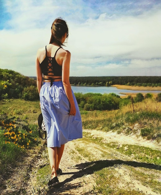 Hintergrundansicht einer Frau, die auf dem Feld gegen den Himmel geht