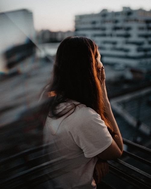 Hintergrundansicht einer Frau, die auf einem Balkon gegen eine städtische Stadt steht