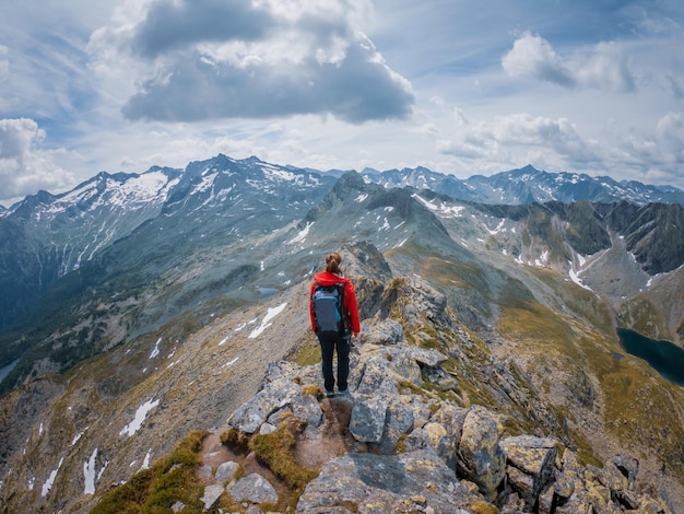 Hintergrundansicht einer Frau, die auf einem felsigen Berggipfel gegen den Himmel wandert