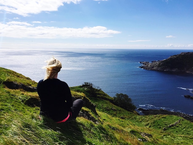 Hintergrundansicht einer Frau, die auf einem Hügel gegen das Meer sitzt