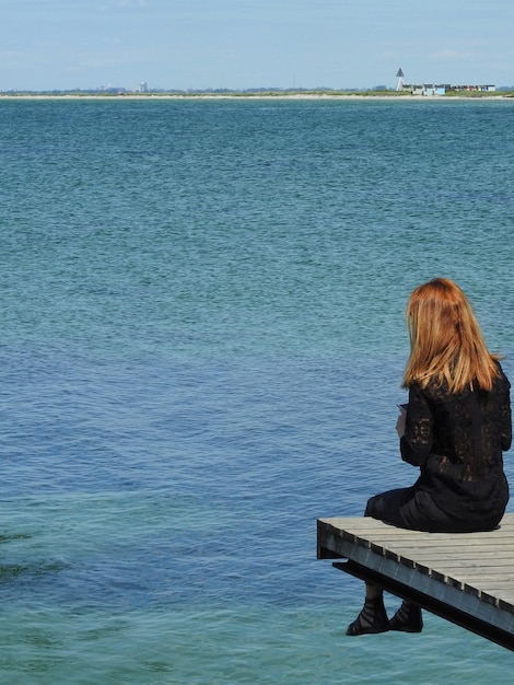 Foto hintergrundansicht einer frau, die auf einem pier über dem meer gegen den himmel sitzt