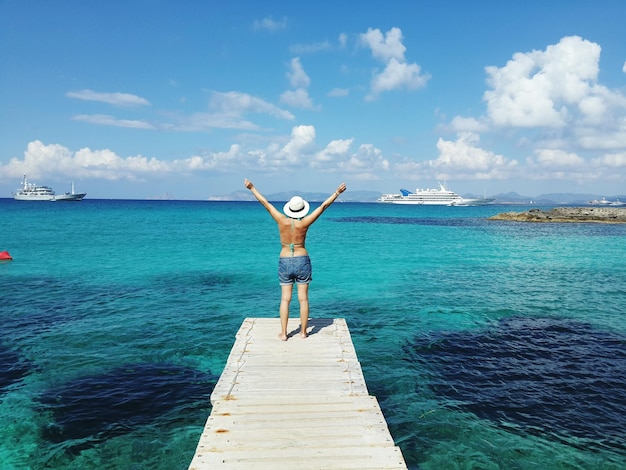 Hintergrundansicht einer Frau, die auf einem Pier über dem Meer gegen den Himmel steht