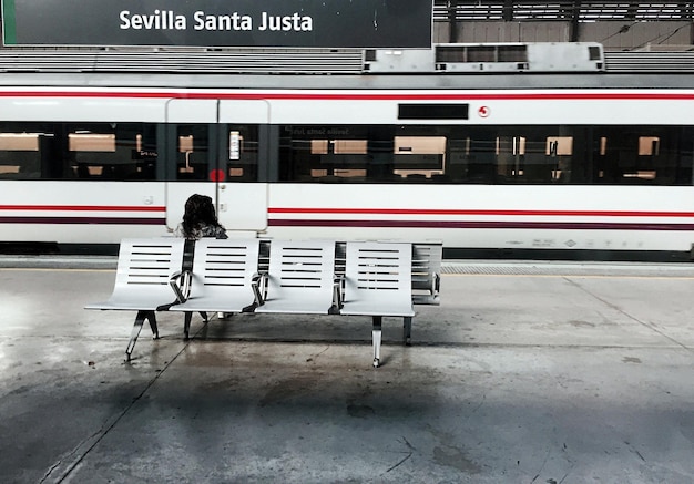 Foto hintergrundansicht einer frau, die auf einem sitz am bahnhofssteig sitzt