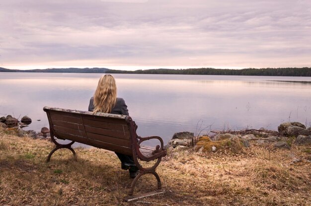 Foto hintergrundansicht einer frau, die auf einer bank gegen den see sitzt