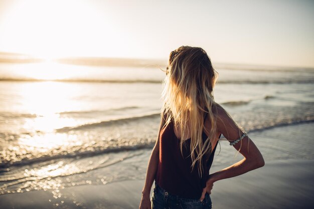 Foto hintergrundansicht einer frau, die bei sonnenuntergang am strand steht