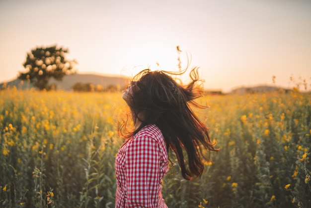 Hintergrundansicht einer Frau, die bei Sonnenuntergang auf dem Feld gegen den Himmel steht