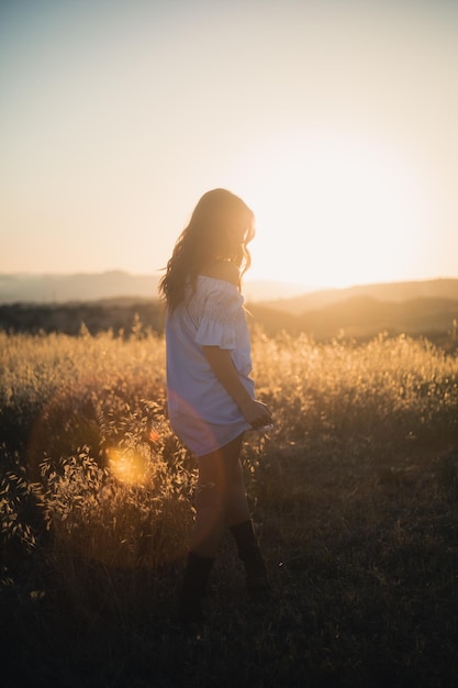 Hintergrundansicht einer Frau, die bei Sonnenuntergang auf dem Feld gegen den Himmel steht