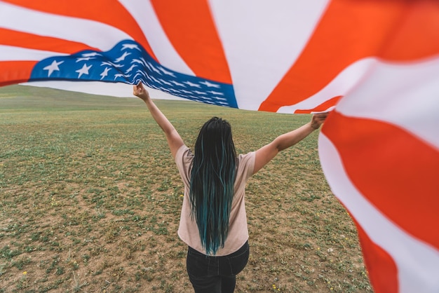 Hintergrundansicht einer Frau, die draußen die amerikanische Flagge hält