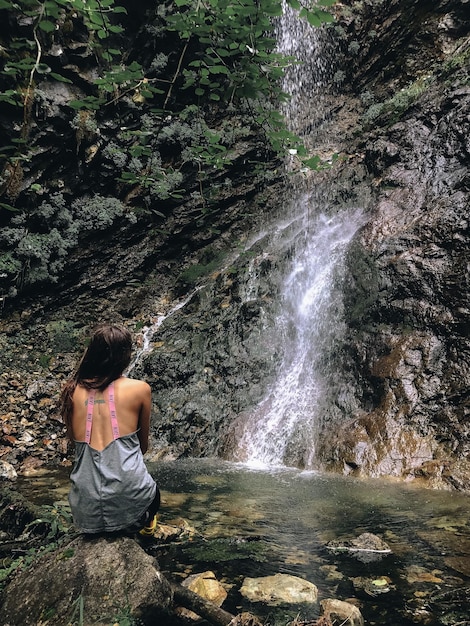 Hintergrundansicht einer Frau, die einen Wasserfall betrachtet.