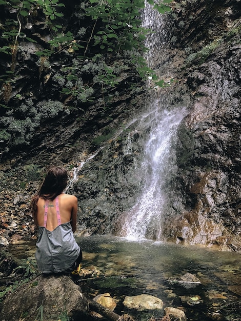 Foto hintergrundansicht einer frau, die einen wasserfall betrachtet.