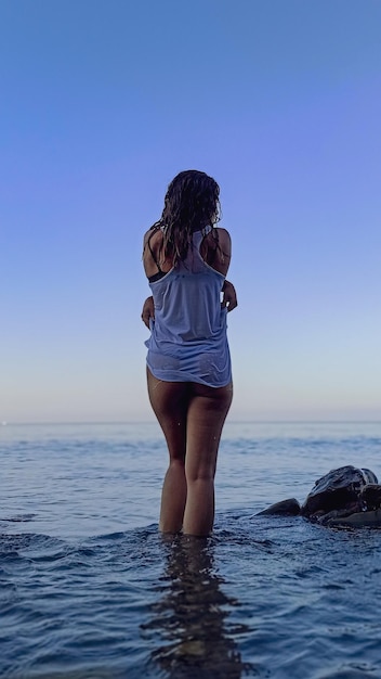 Hintergrundansicht einer Frau, die im Meer gegen einen klaren Himmel steht