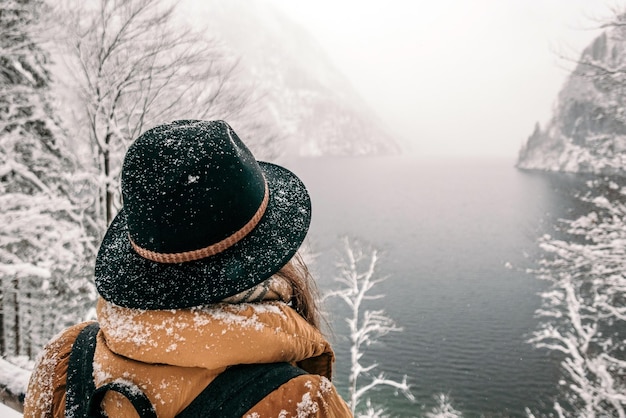 Foto hintergrundansicht einer frau, die im winter auf einem aussichtspunkt über dem see steht, während sie auf einer wanderung in der schnee-natur ist