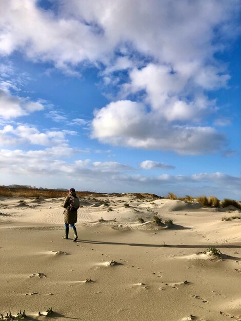 Foto hintergrundansicht einer frau, die unter weißen wolken und der aufgehenden sonne durch eine dünenlandschaft geht