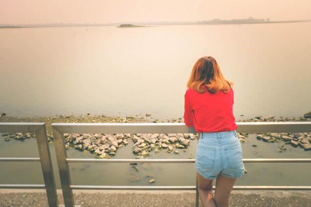 Foto hintergrundansicht einer frau, die vom zaun aus auf das meer schaut