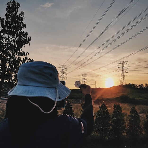 Foto hintergrundansicht einer frau, die während des sonnenuntergangs eine blume gegen den himmel hält