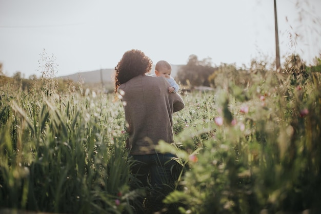 Foto hintergrundansicht einer frau mit einem baby, die auf dem feld gegen den himmel läuft