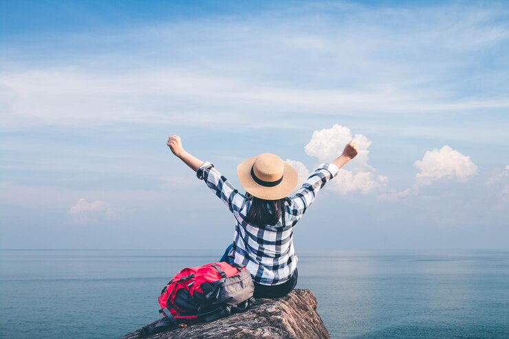 Foto hintergrundansicht einer frau mit erhobenen armen, die auf einer klippe am meer gegen einen bewölkten himmel sitzt