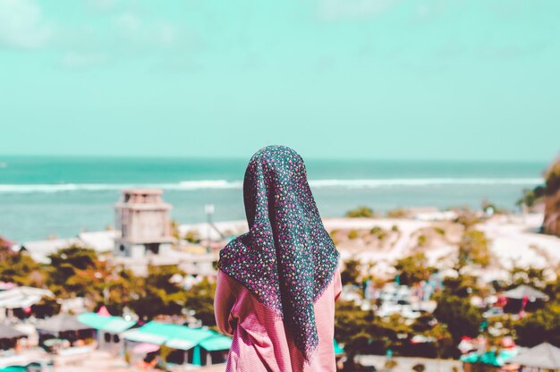 Hintergrundansicht einer Frau mit Hijab, die am Strand steht und auf die Aussicht schaut