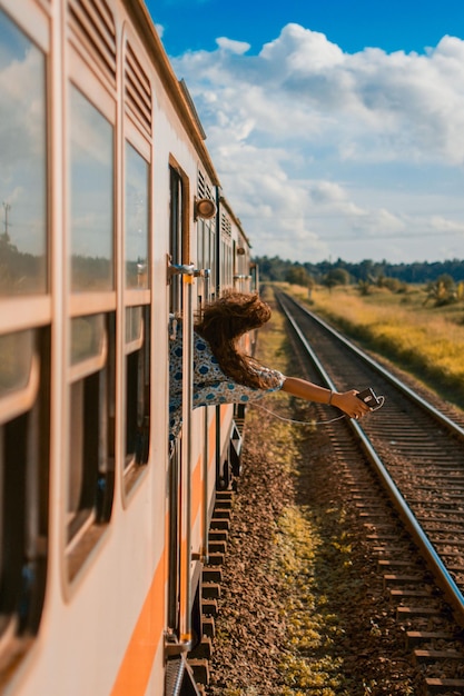 Hintergrundansicht einer glücklichen Frau mit Handy, die während einer Zugfahrt durch das Fenster schaut