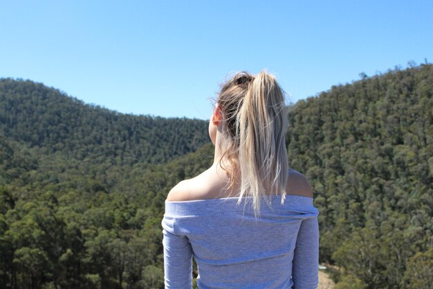 Foto hintergrundansicht einer jungen frau, die auf einem berg gegen einen klaren blauen himmel steht