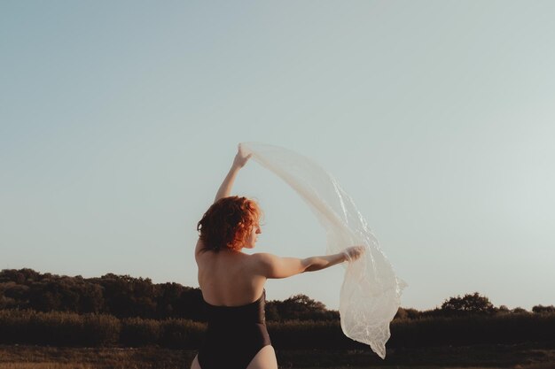 Foto hintergrundansicht einer jungen frau, die plastik hält, während sie vor klarem himmel auf dem land steht