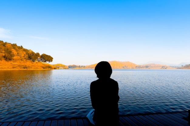 Hintergrundansicht einer Silhouette-Frau, die auf den See gegen den Himmel schaut