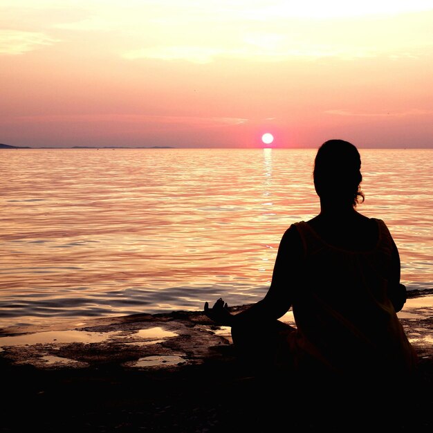 Foto hintergrundansicht einer silhouette von einer frau, die bei sonnenuntergang am meer meditiert